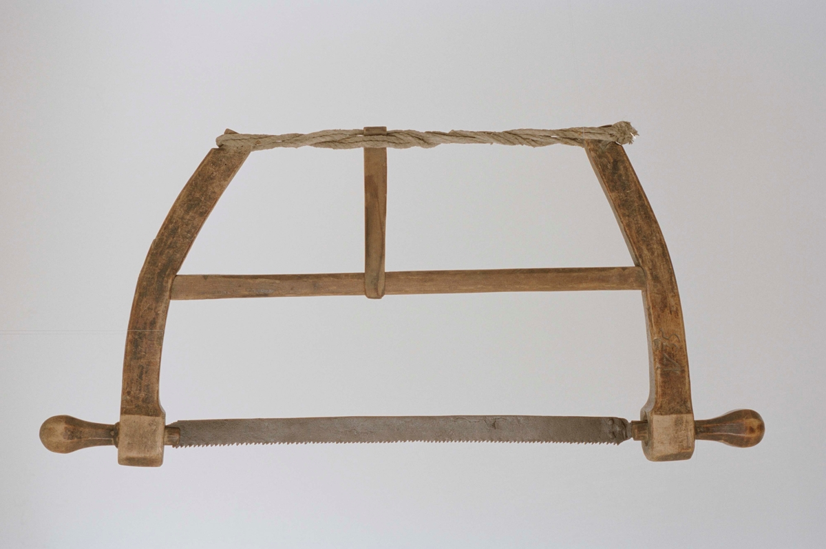 Tvåhandsfattad såg, lätt bågformad ram med tvärslå, hålls ihop upptill med tvinnat rep. Märkt " 1735 ".