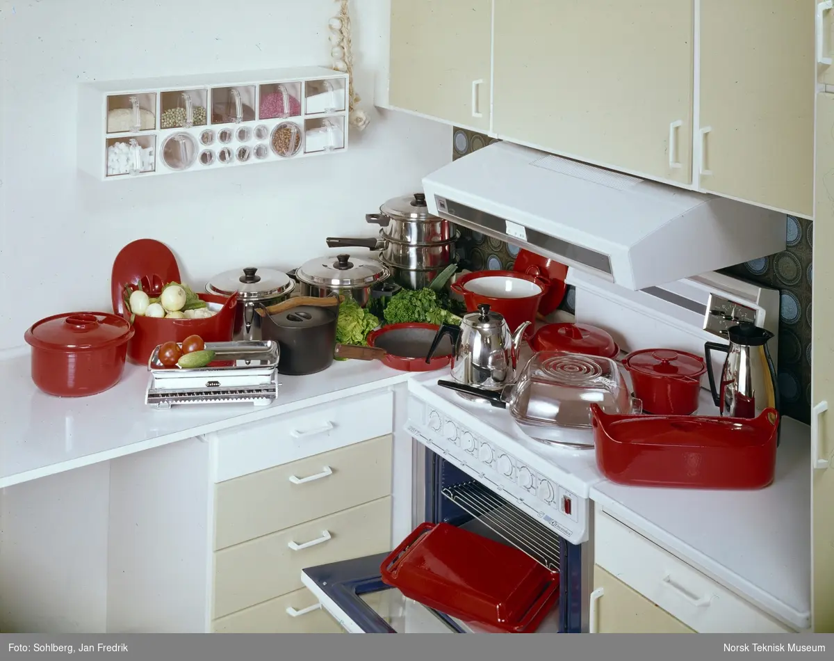Et velutrustet kjøkken med diverse kjøkkenutstyr; røde og blanke kjeler, kasseroller, panner, kanner og fat.