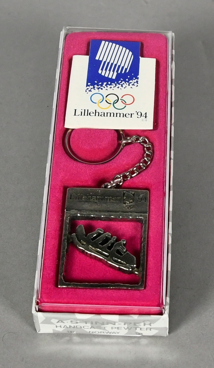 Nøkkelring med rektangulært anheng med piktogram for bob. Nøkkelringen ligger i original emballasje på rosa underlag.