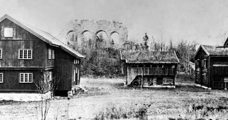 Svart-hvitt foto av bygningene på Hedmarkstunet nedenfor domkirkeruinen.