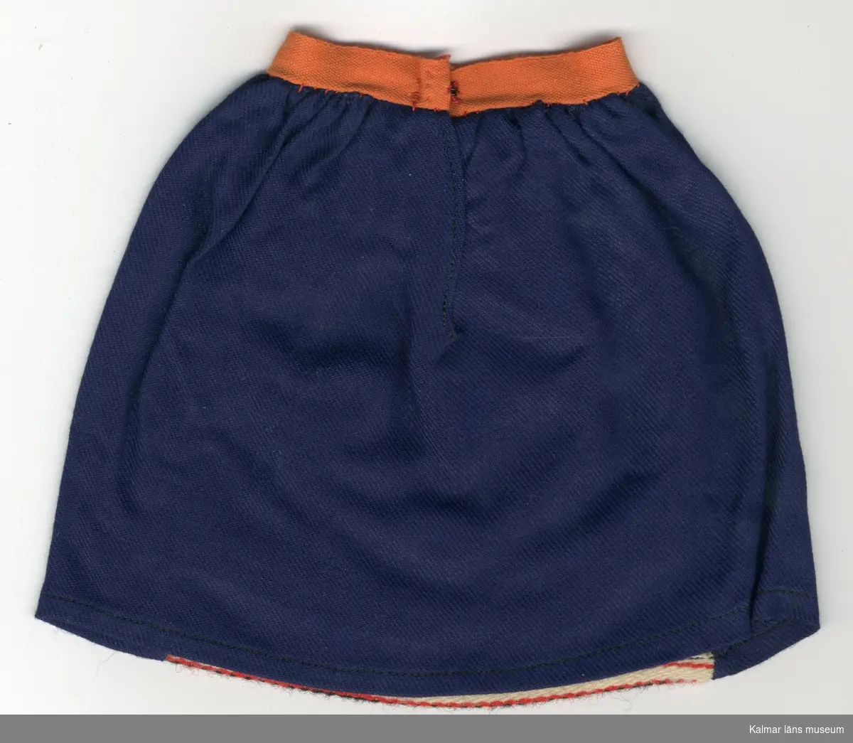 KLM 28082:266:1-4 Dockkjol, del av dräkt, av textil, ylle och bomull. Kjol, blå med infällt förkläde, av ylle, lodräta ränder i svart, rött, grönt, vitt och orange färg, Kjol och förkläde rynkade. :2 och :4 kjolar har bomullsband i orange färg i linning, :1 och :3 kjolar har bomullsband i ljusrött i linning. Knäppning, alla plagg, med en  hyska, av röd tråd och en hake, av metall. :1 Kjol har etikett fäst vid fåll, med texten: 19- (i blyerts). Nationaldräktskjol från Rättvik.