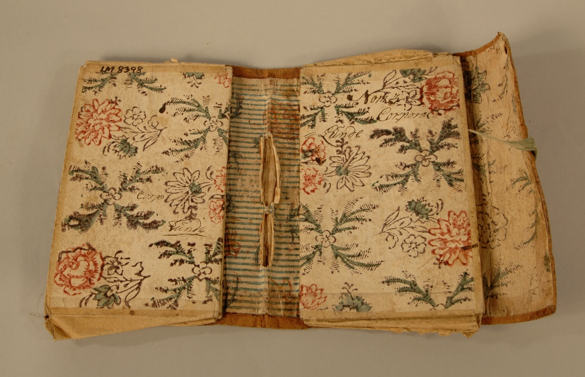 Lommebok i skinn, med innvedige rom i papp som er kledd med papir med blomstermotiv.