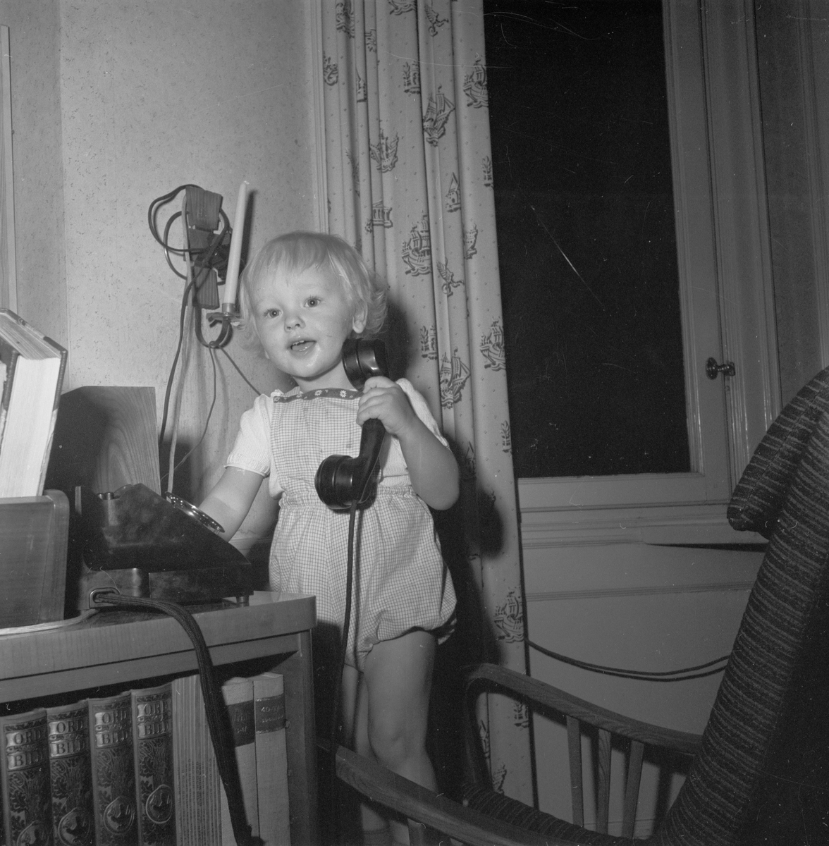 Pojke står i fåtölj och leker med en telefon, Uppsala 1952