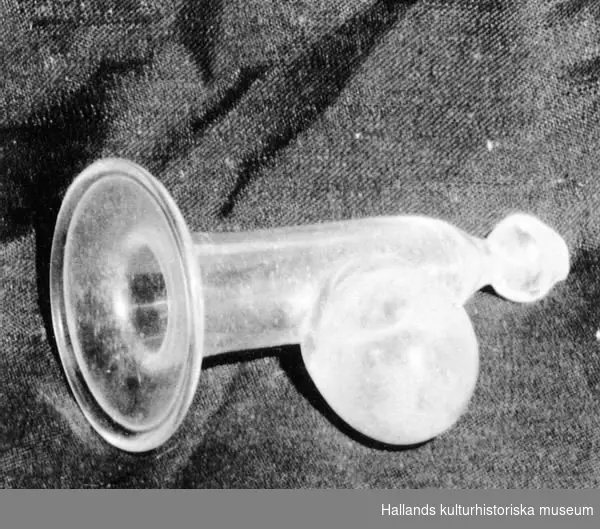 Bröstpump av glas. Trumpetformat glas med klotformig behållare tillfogad på undersidan. Tillhörande gummiblåsa saknas.