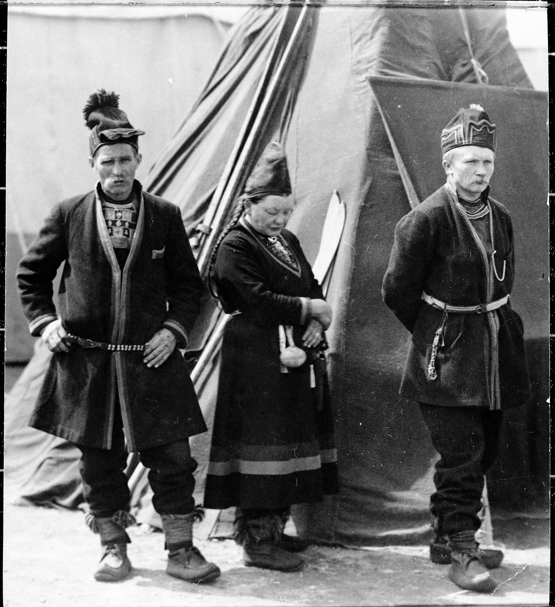 To menn og ei dame i samiske drakter foran telt