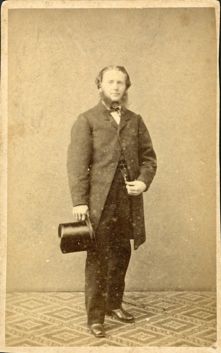 Ateljéporträtt av oidentifierad man med polisonger klädd i jackett, hållande en cylinderhatt