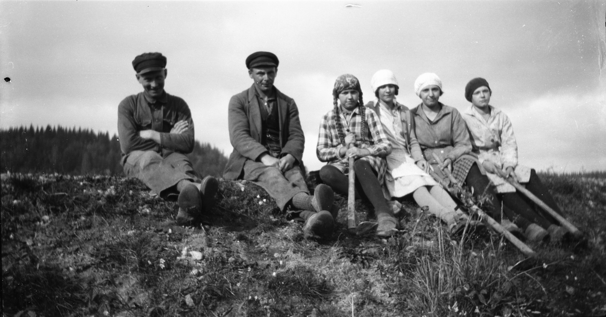 Bygdefotografen "Kloar-Erik" har själv satt sig framför kameran tillsammans med fyra unga kvinnor med hackor och en man med armarna i kors. De sitter på kanten av en grusig slänt. En av flickorna har långa flätor.