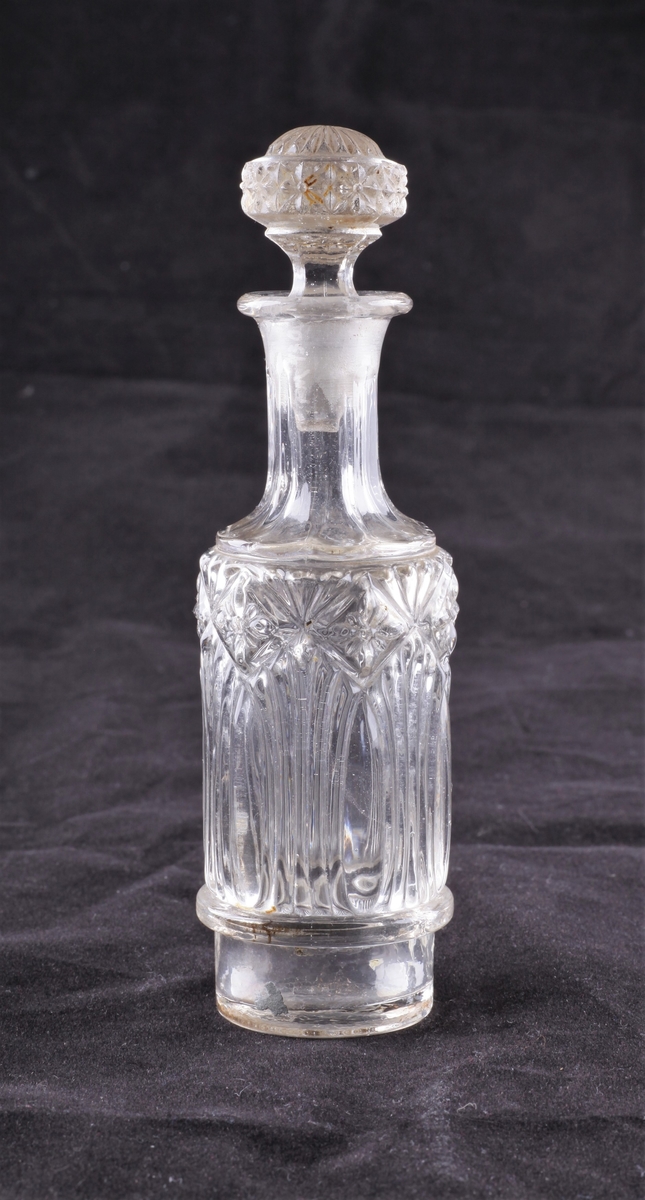 Flasken er regelmessig rund med slank hals og har en glasspropp. Flasken er dekorert med vertkale linjer, og blomster innrammet av ruter øverst. Glassproppen har en lignende blomsterkrans.