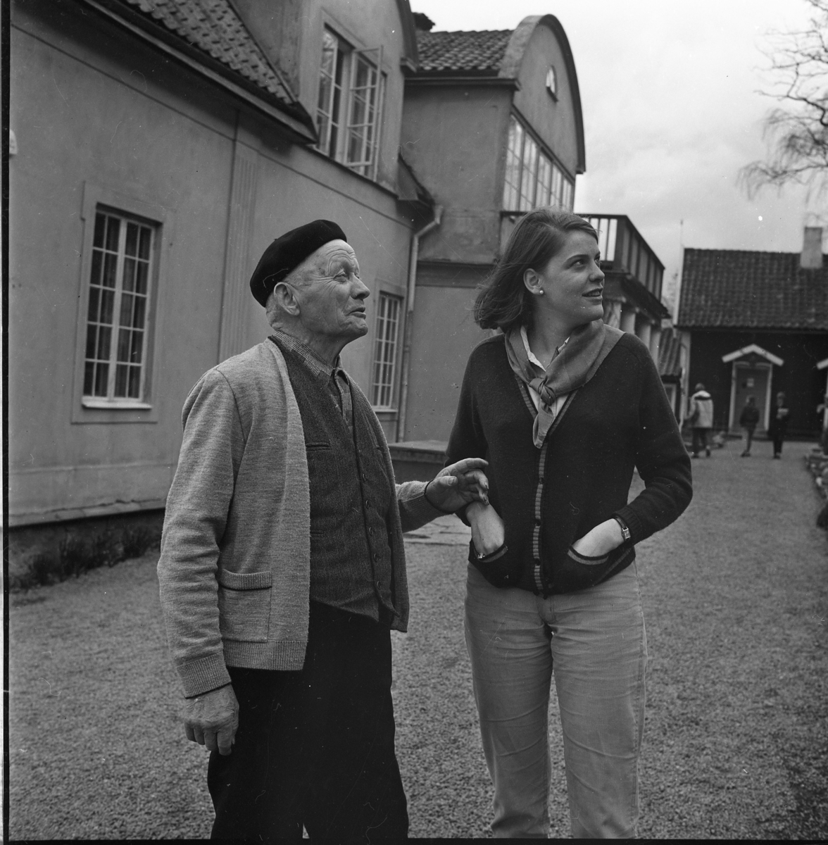Trädgårdsmästare Ernst Stark med basker på huvudet står i trädgården till Borgmästargården med en ung kvinna.