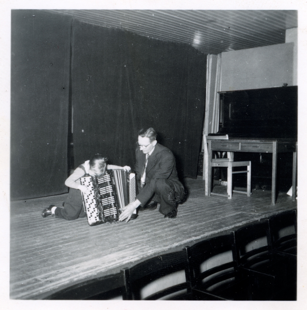 En pojke och en man sitter på en scen med ett dragspel.