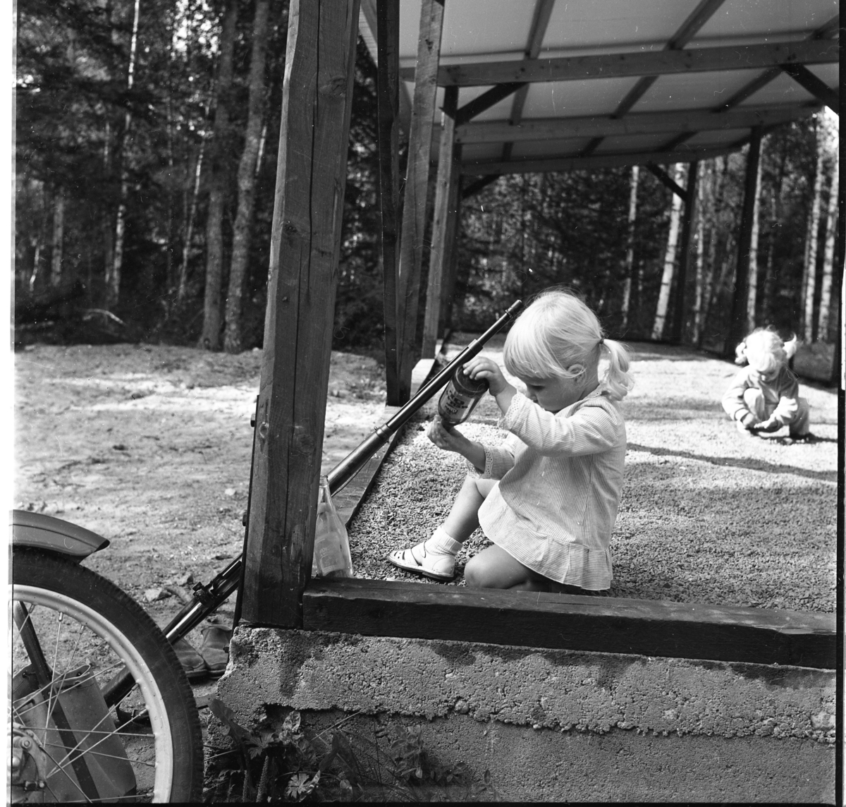 Två små flickor leker på vallen till en skjutbana. Ett gevär står lutat intill flickan i förgrunden.