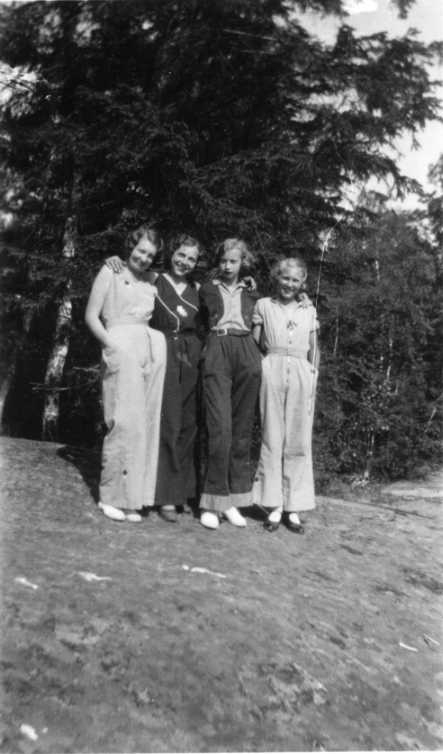 Fyra unga kvinnor i byxdress står tätt intill varandra med armarna runt varandras hals. De är från vänster Ingrid Hellberg, okänd, Britta Gustavsson samt okänd.