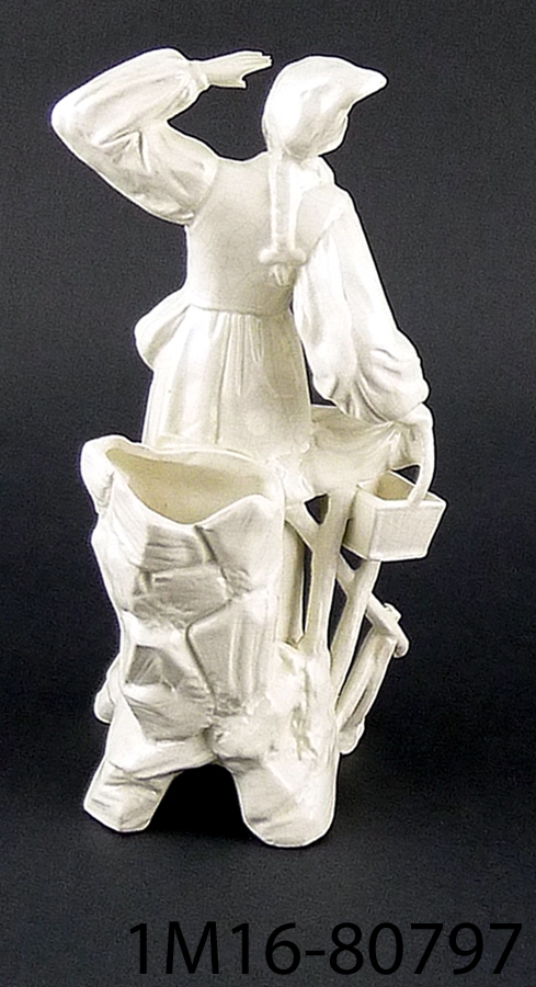 Staty av porslin, vit, kvinna som i högra handen håller en korg och skuggar för ögonen med vänster hand.