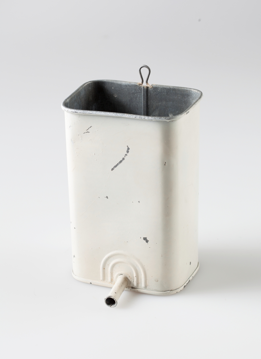 Hvitmalt beholder i sink med hempe for oppheng. Et rør nederst på beholderen koples til en gummislange med spiss for bruk til klyster.