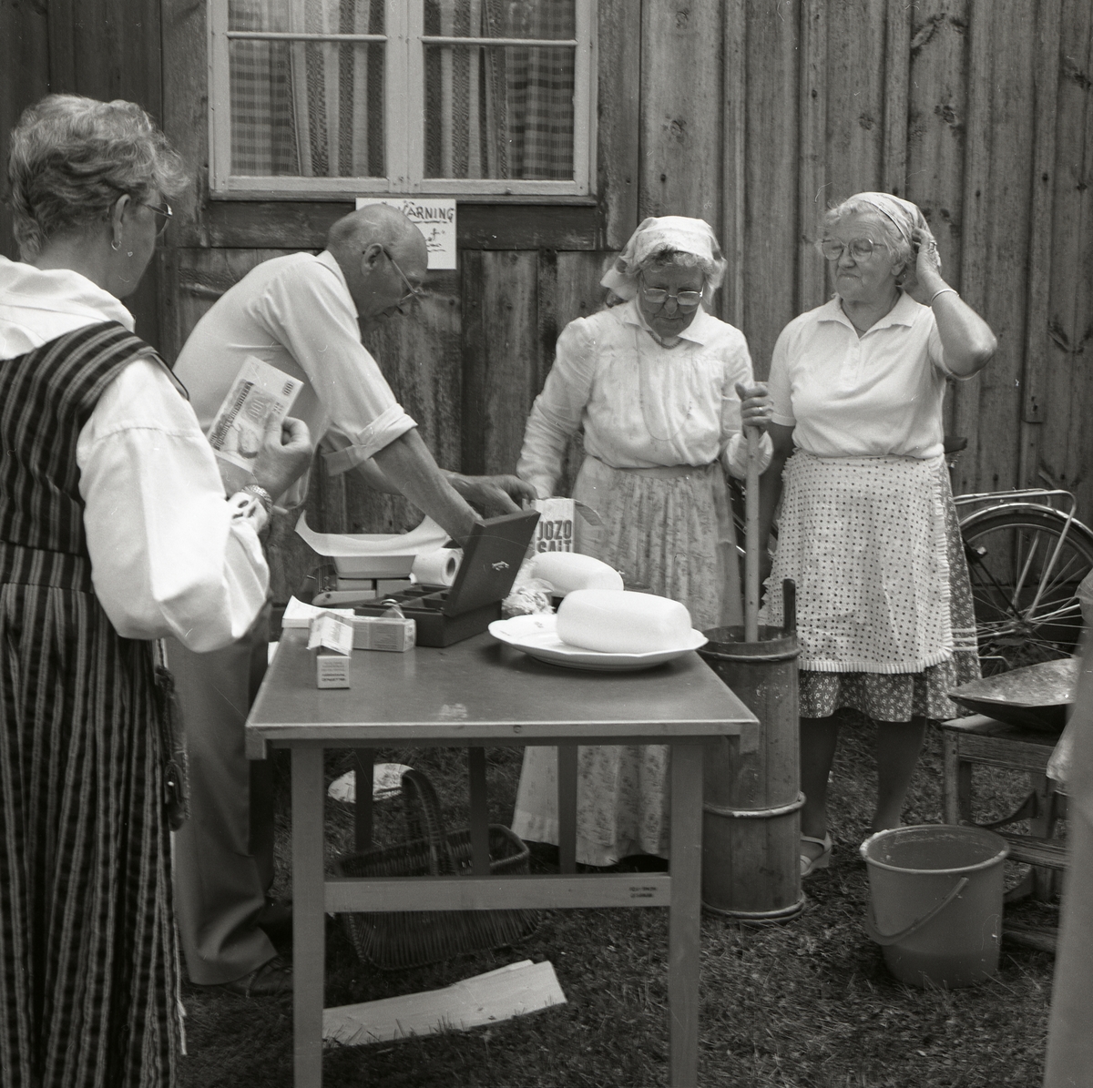 Försäljning av bakverk på Rengsjöfesten, 14 juli 1985. Intill försäljningsbordet kärnar två kvinnor smör.