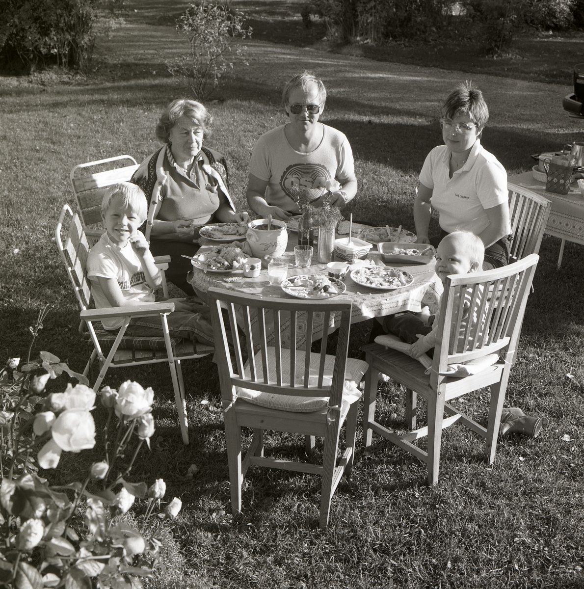 Fem personer sitter vid ett bord i en trädgård och äter middag, 6 oktober 1985.