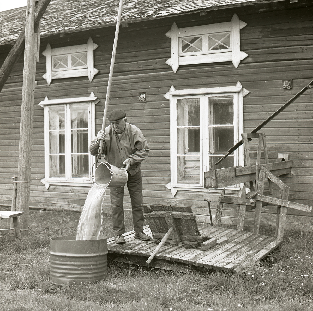 En man häller ut en hink med vatten i ett kärl, Bredvik 1974.