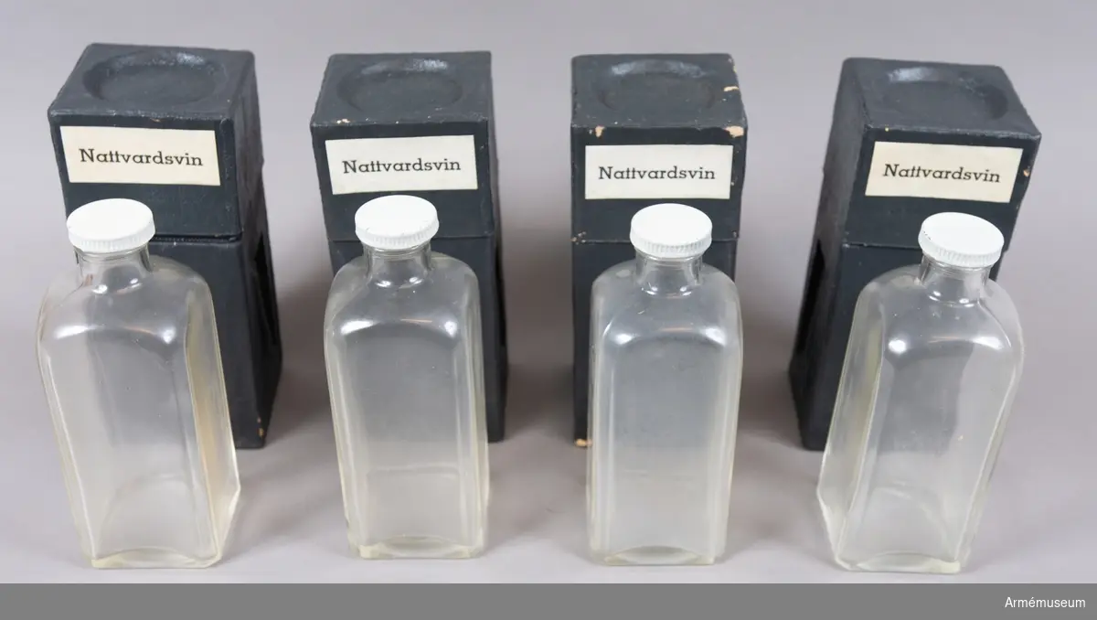 Fyra stycken glasflaskor med skruvlock i metall förvarade i fyra separata transportfodral av svart papp. Fodralen är förpackade i en kartong märkt med etiketten "Nattvardsvin".