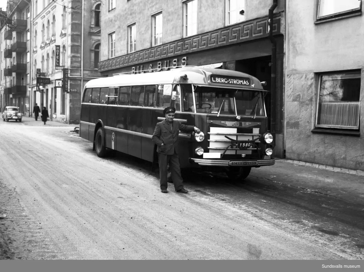 En ny buss levereras till L. Berg, Strömås, utanför Bil & Buss vid Köpmangatan 12. Chauffören står utanför.