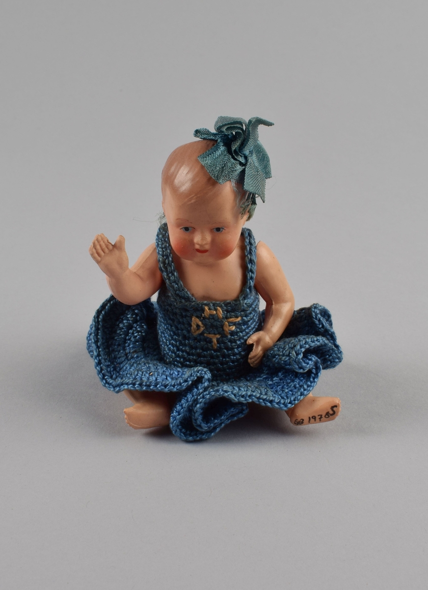 Liten figur av jente med heklet kjole og skøyfe i håret. Bevegelige armer og ben festet med innvendig tråd.