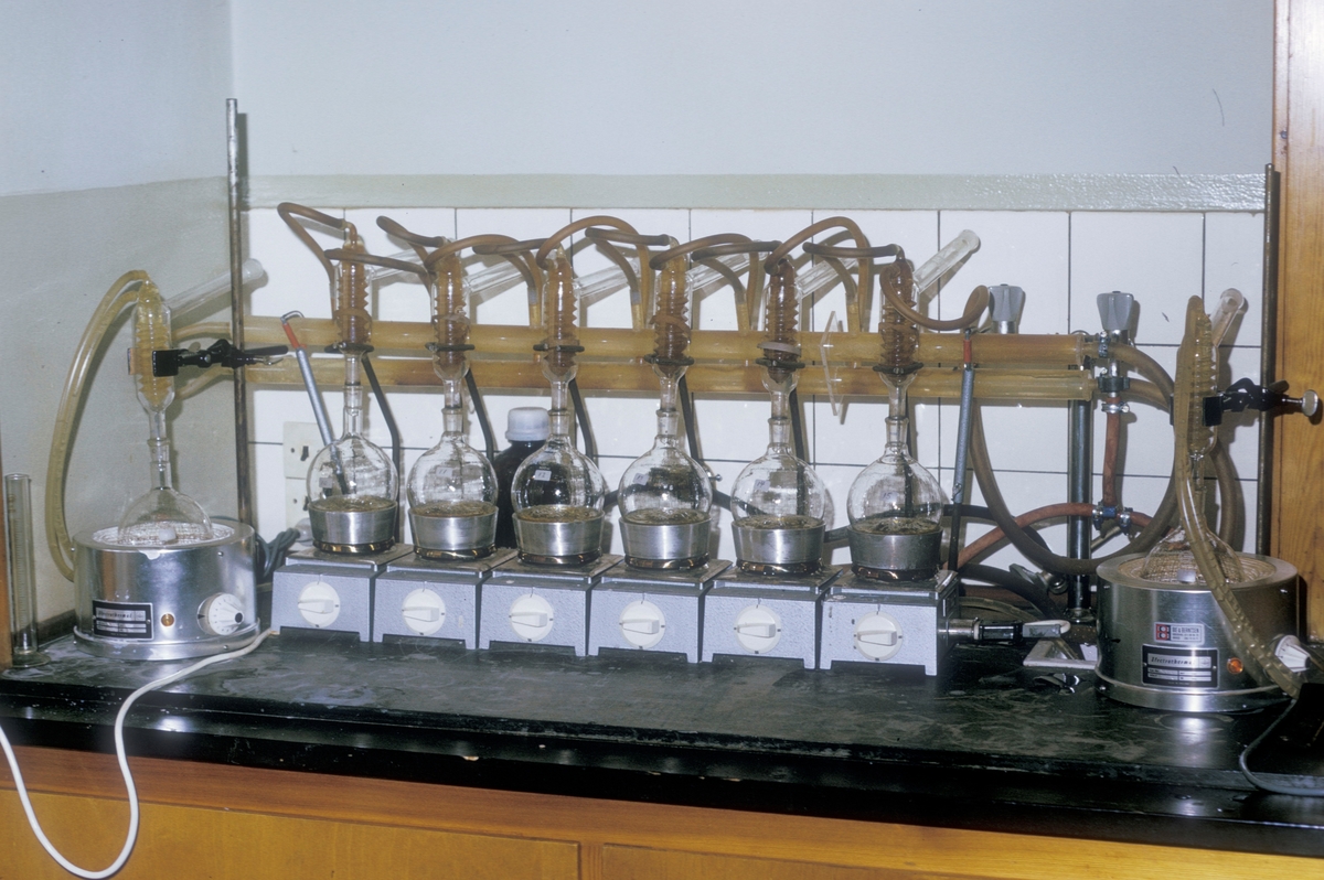 Forsøgsdambruget i Brøns, Danmark, 1974 : Laboratorium med diverse apparater, glass og instrumenter på en arbeidsbenk.