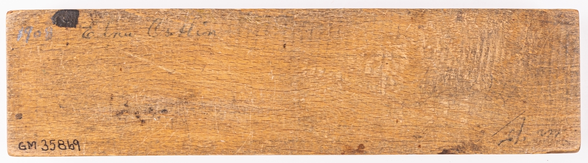 Pennskrin av trä med skjutlock. På locket en målad pensé. På undersidan står: 1908 elna Östlin. I skrinet ligger tre pennstift av metall.