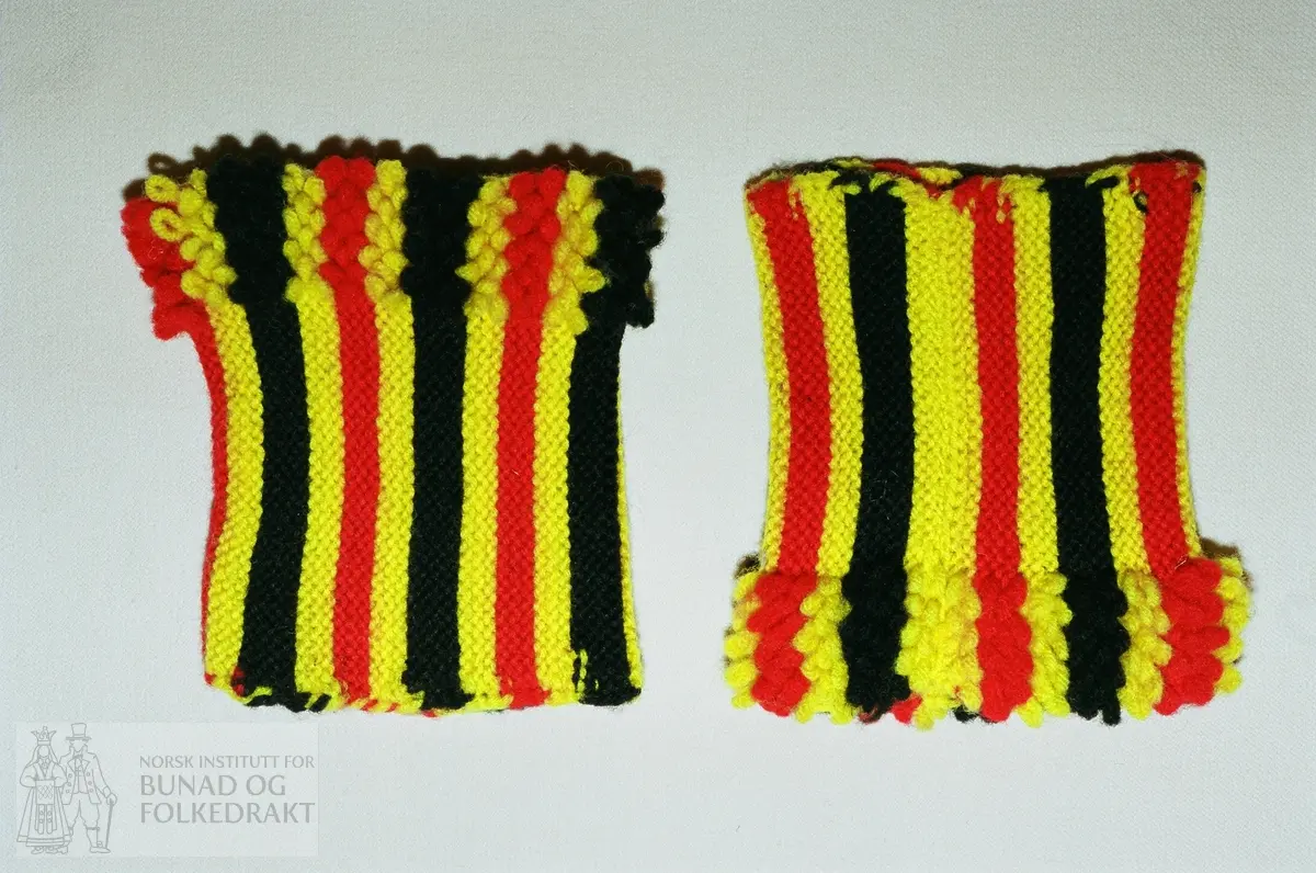 Rillestrikka rett i striper med gult, rødt og svart firetrådet ullgarn. Hver stripe har tre riller. I ene enden er det strikka inn løkker, 4 løkker som er strikka inn ved annenhver maske. Høgde ring:        ca 10,5 cm. Bredde løkkekant:  2,5-3,0 cm.