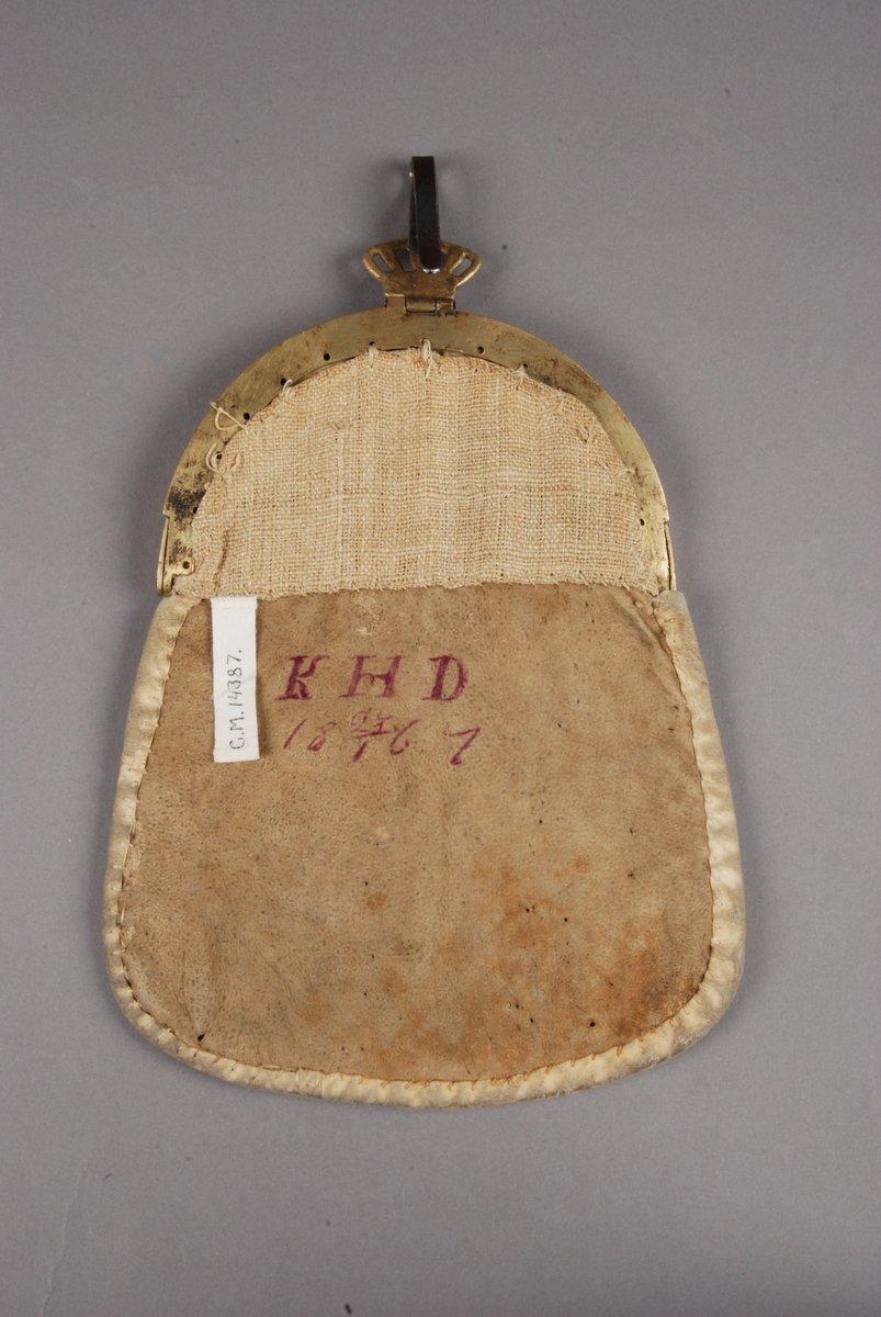 Väska med svart ylle med applikatikoner i rött och grönt, tenntrådsbroderi. Spänne av mässing.
Baksidan märkt: KHD 1867.