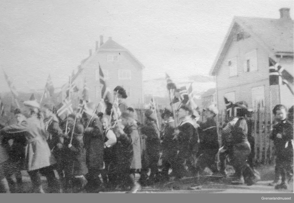 Hans Majestet Kong Haakon VII på kongebesøk i Kirkenes, sannsynlisgvis i juni 1922. Masse barn med norske flagg går i tog for kongen.