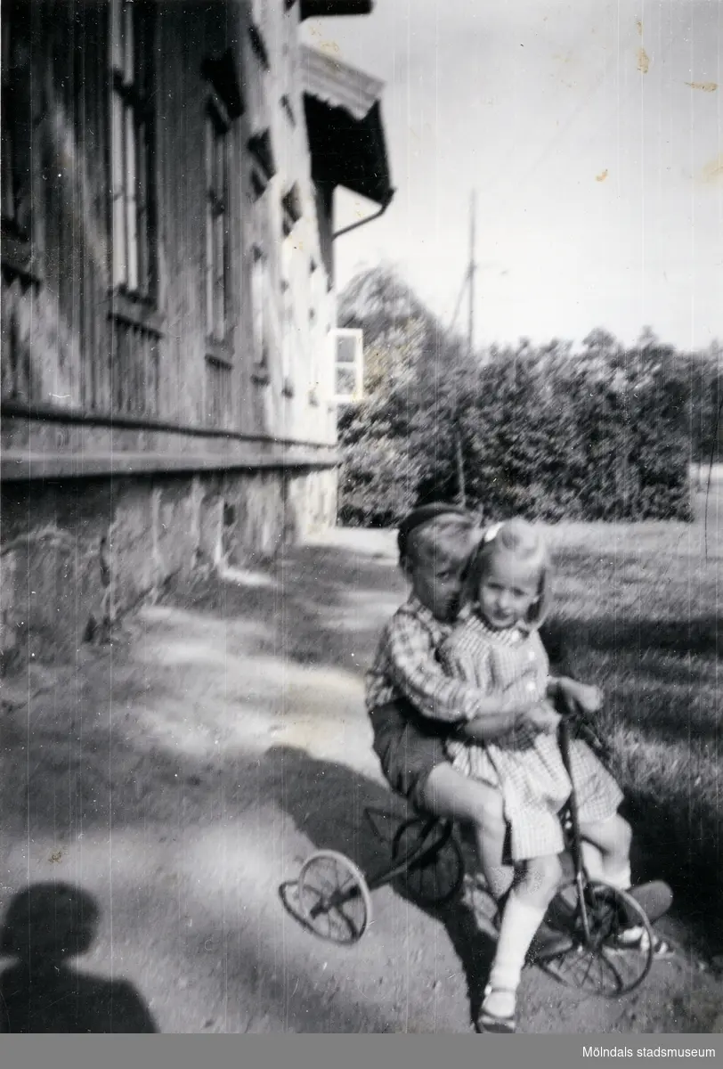 En pojke, Stig-Arne Johansson, och en flicka sitter på en trehjuling vid mangårdsbyggnaden till gården Christinedal i östra Mölndal på 1950-talet. Gården har gett namn åt området Kristinedal och var belägen i vinkeln mellan nuvarande Rådavägen och Brovaktaregatan. År 1960 såldes gården till Fastighetsbolaget Betongblandaren (Skånska Cementgjuteriet) och revs när det nuvarande bostadsområdet anlades.