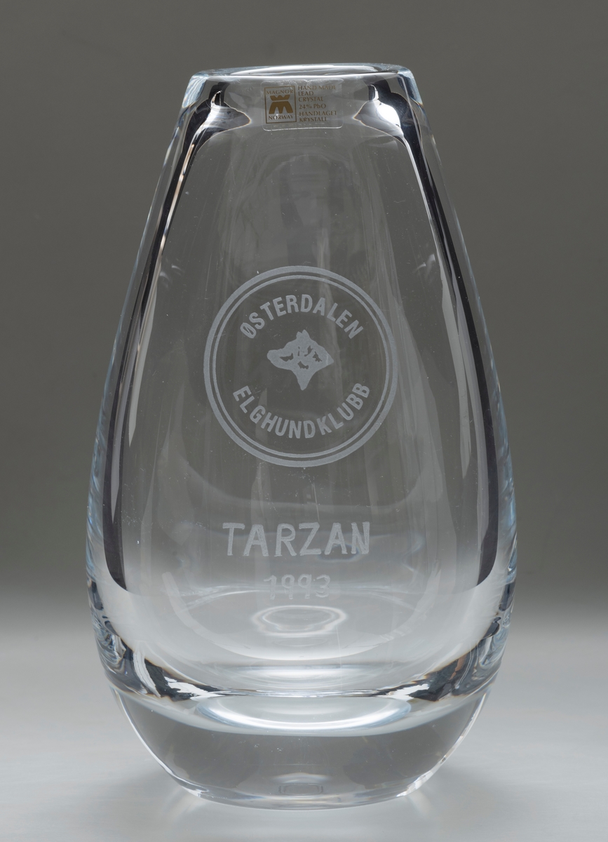 Oval vase i glass, krystall, som er bredest litt under midten. På den ene siden: innskriften TARZAN / 1993 (med emblemet til Østerdalen Elghundklubb over).