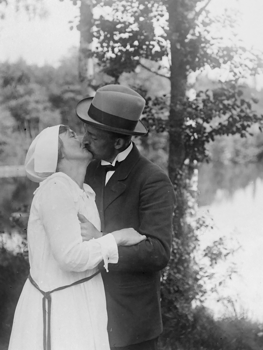 Fästfolket Hanna och Anders kysser varandra, bakom dem syns några träd och en sjö