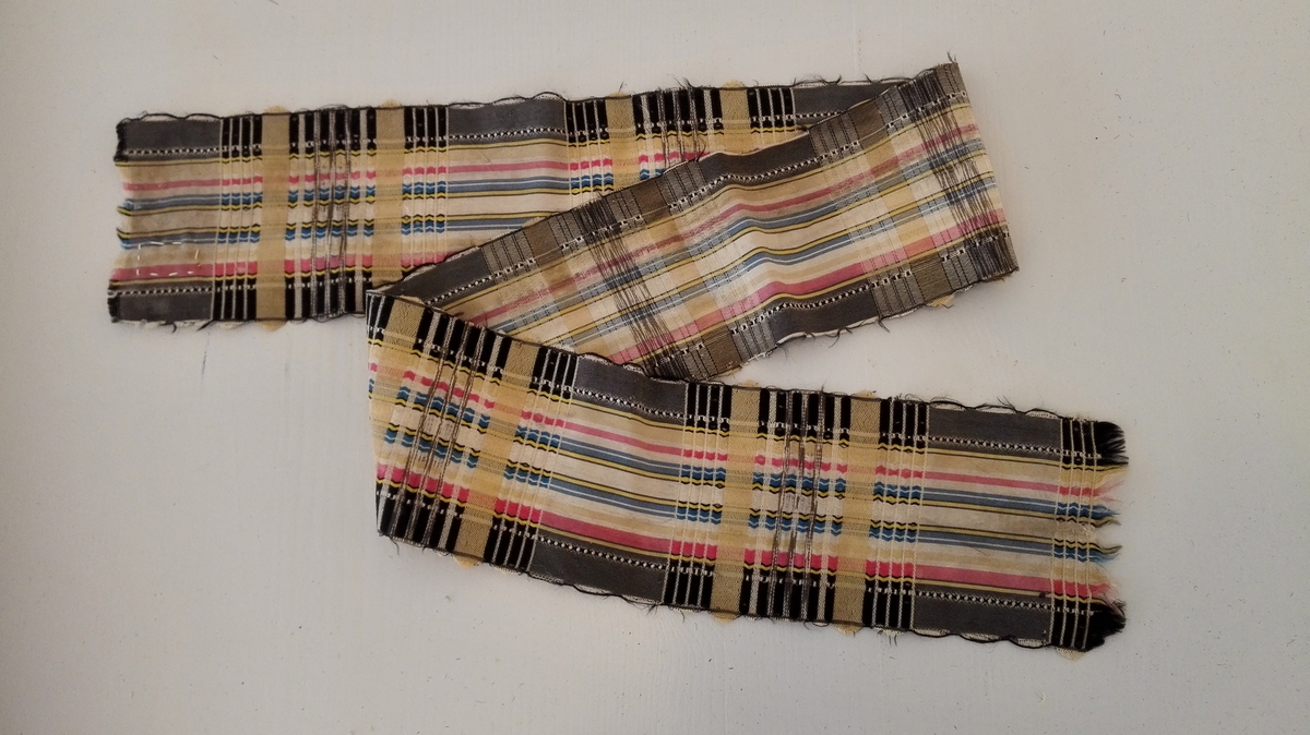 1 silkebånd

Silkebånd, 6,8 cm bredt og 68 cm langt. Vevet i langs- og tversgående striper i sort, grått, rødt, blått og gult.

Gave fra fru Laura Finckelsen f. Hjortdahl, Oslo