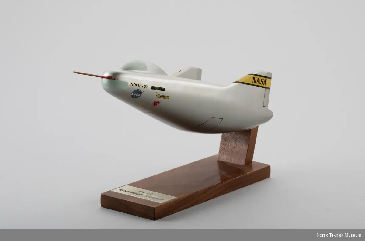 Liten sølvfargert flymodell montert på bordstativ av tre