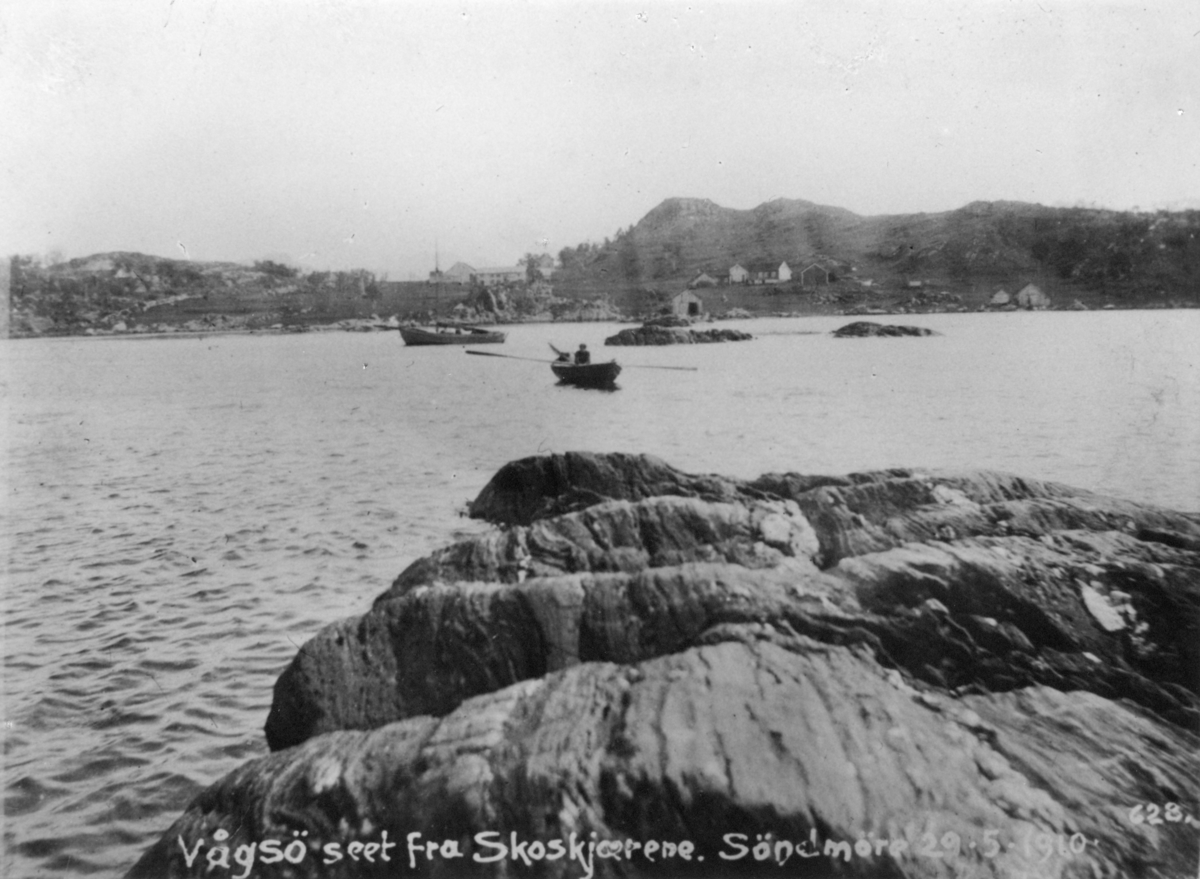 Motiv av Vågsøy sett fra Skoskjærene. To trebåter ligger på sjøen i forgrunnen.