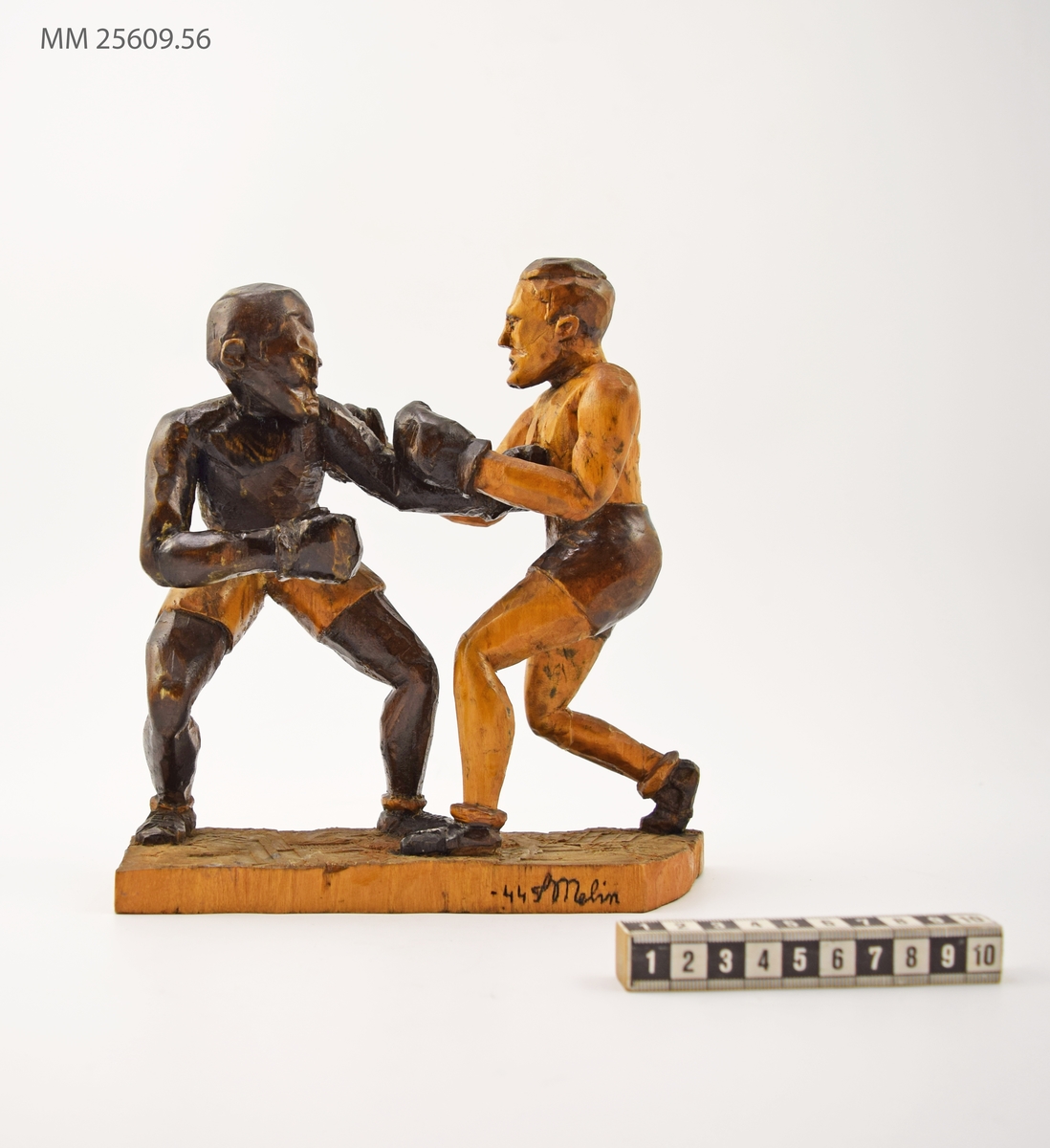 Statyett i snidat trä som föreställer två boxare i match mot varandra. I ögonblicket konstnären fångat dem får den vänstra boxaren in ett slag i magen på den högra. Boxarna är klädda i shorts och boxarskor. Statyetten fernissad.