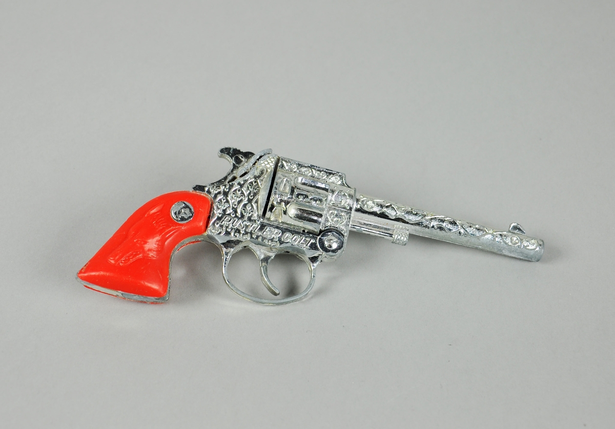 Blank revolver med dekor i relieff, og med rødt plastikkskjefte med et ulvehode i relieff.
