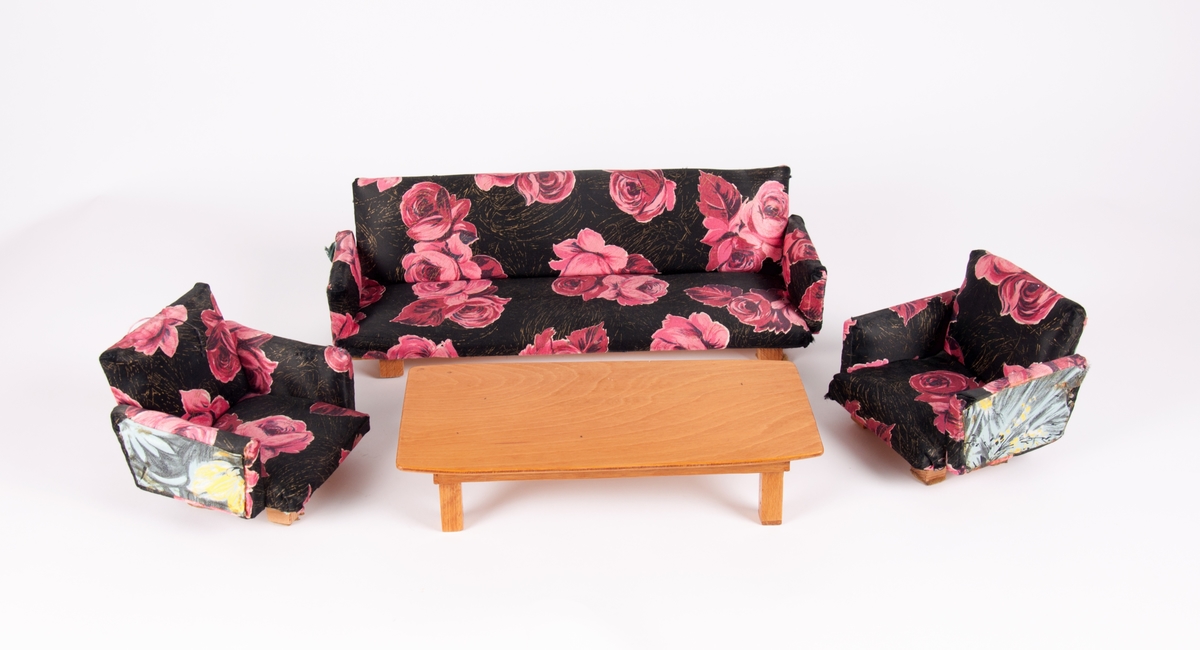 Dukkemøbler, sofa, bord og to stoler. Sofa og stoler er polstret og trukket med blomstret trekk. Bord av lakkert kryssfiner.