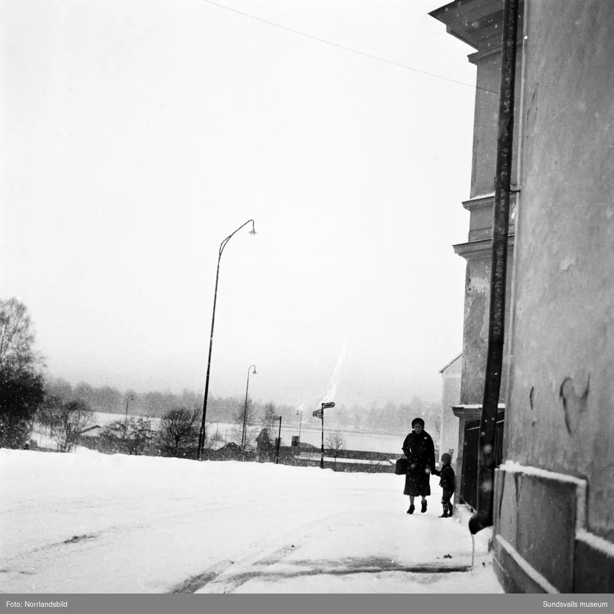 En kvinna med ett barn i handen promenerar i snöovädret Sidsjövägen söderut invid Grönborg.