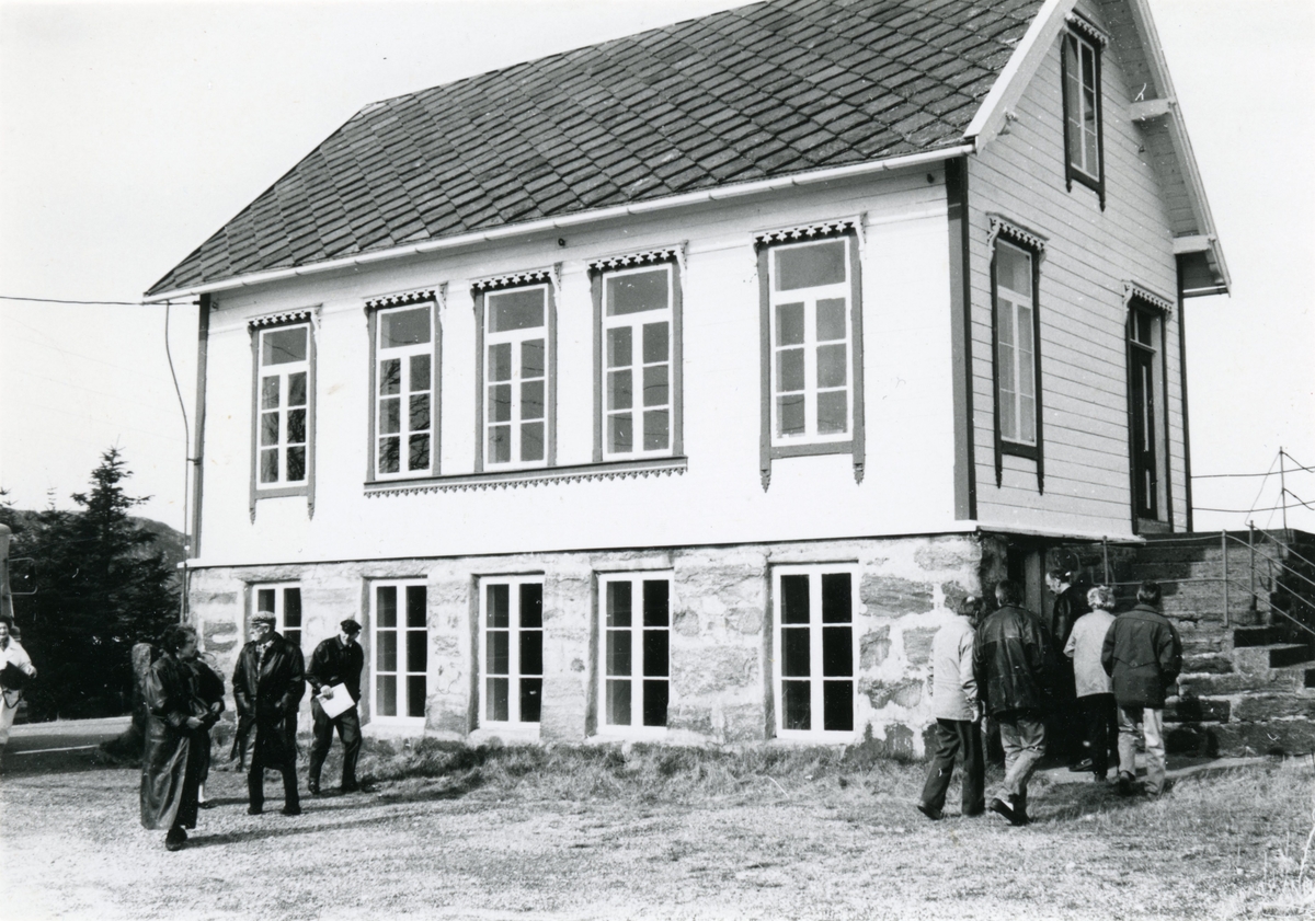 Prospektfotografi av den gamle skulebygninga på Fjørtoft. Utenfor er det flere mennesker på vei inn i bygninga.