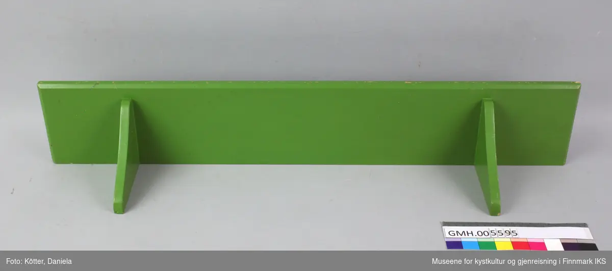Den  grønne trehyllen er laget av et enkelt rektangulært bord med en avrundet kant foran. Under hylla på hver side, er det festet to buede vinkler som smalner nedover. På toppen av hylla bakerst er det skrudd inn øyekrokerl til oppheng.