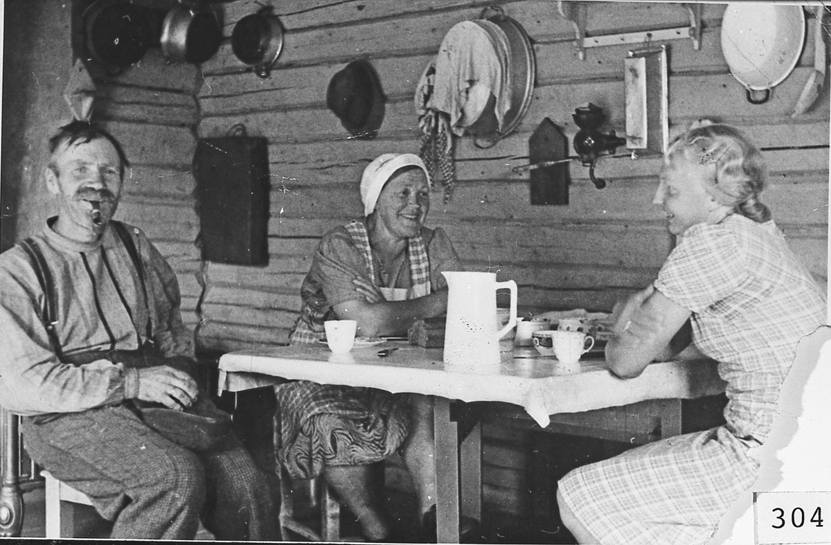 Kaffebesøk i sommerstua på Vatnås, 1944. Mennesker rundt bordet, husgeråd på veggen. 