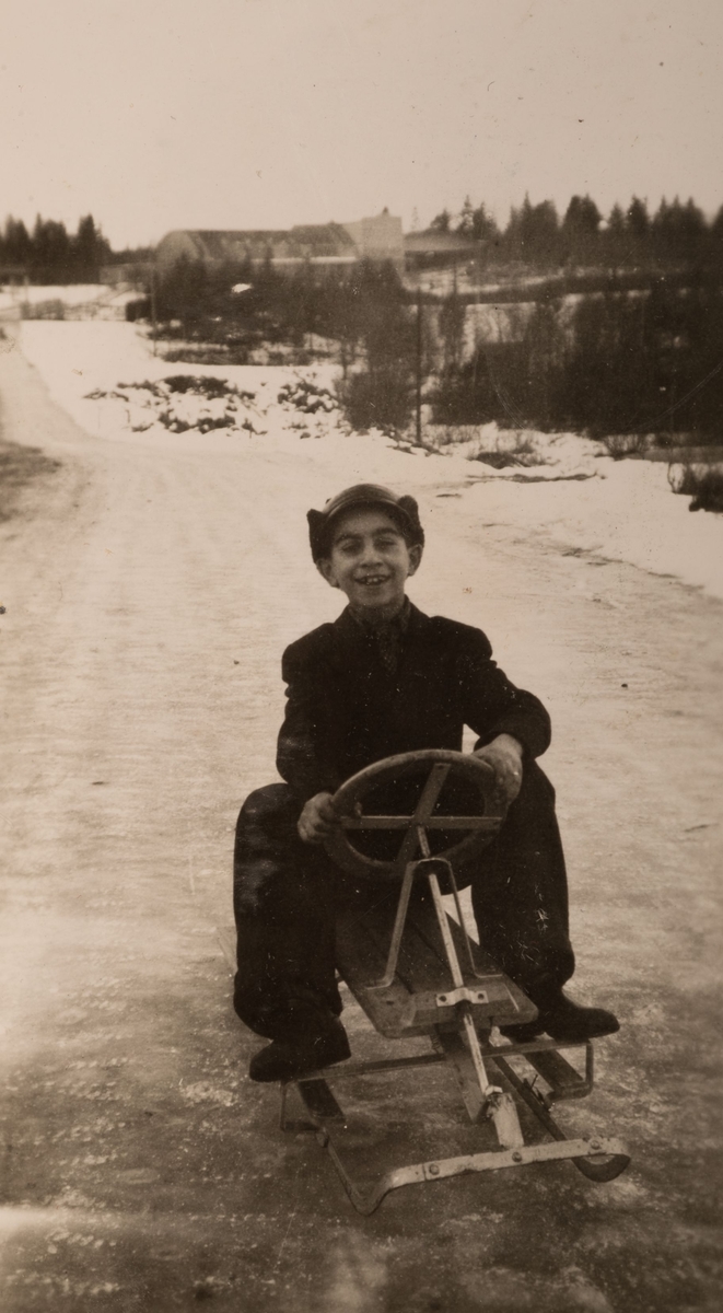 En romsk pojke åker rattkälke på en landsväg i Storvik vintern 1947. I bakgrunden på fotot syns idrottsanläggningen Parkhallen.