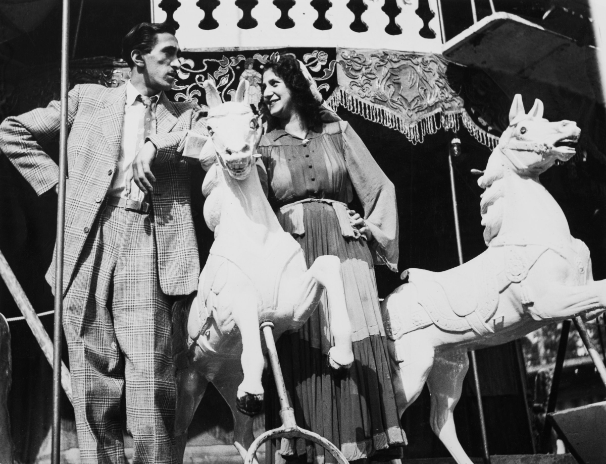 En romsk man och en kvinna står på varsin sida om en karusellhäst och tittar på varandra. Bilden är tagen år 1948.