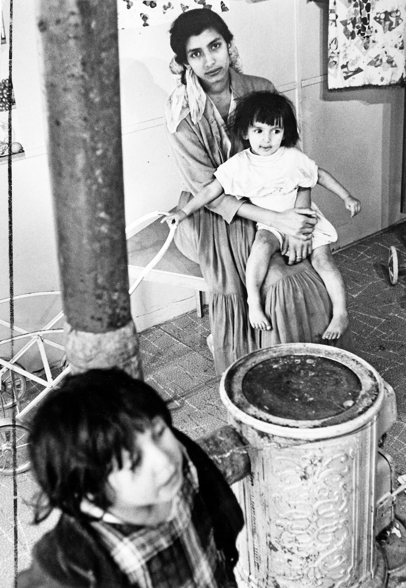 Bilden föreställer en ung mamma och hennes två barn i deras bostadsvagn i det kommunalt inrättade lägret för romer, Ekstrubben, i Stockholm. Lägerplatsen Ekstubben låg i Skarpnäck söder om Stockholm, i nuvarande Flatens naturområde, på en plats där det i dag ligger en motorbana.
