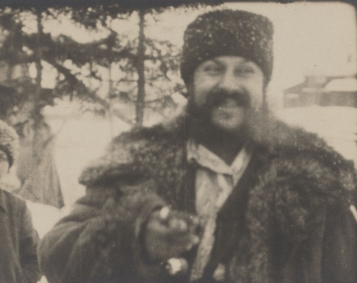 En skrattande kelderashromsk man visar upp något för kameran. Hans väst pryds av stora silverknappar. Mannen är kelderashrom och kom till Sverige med sin familj i slutet av 1800-talet.
