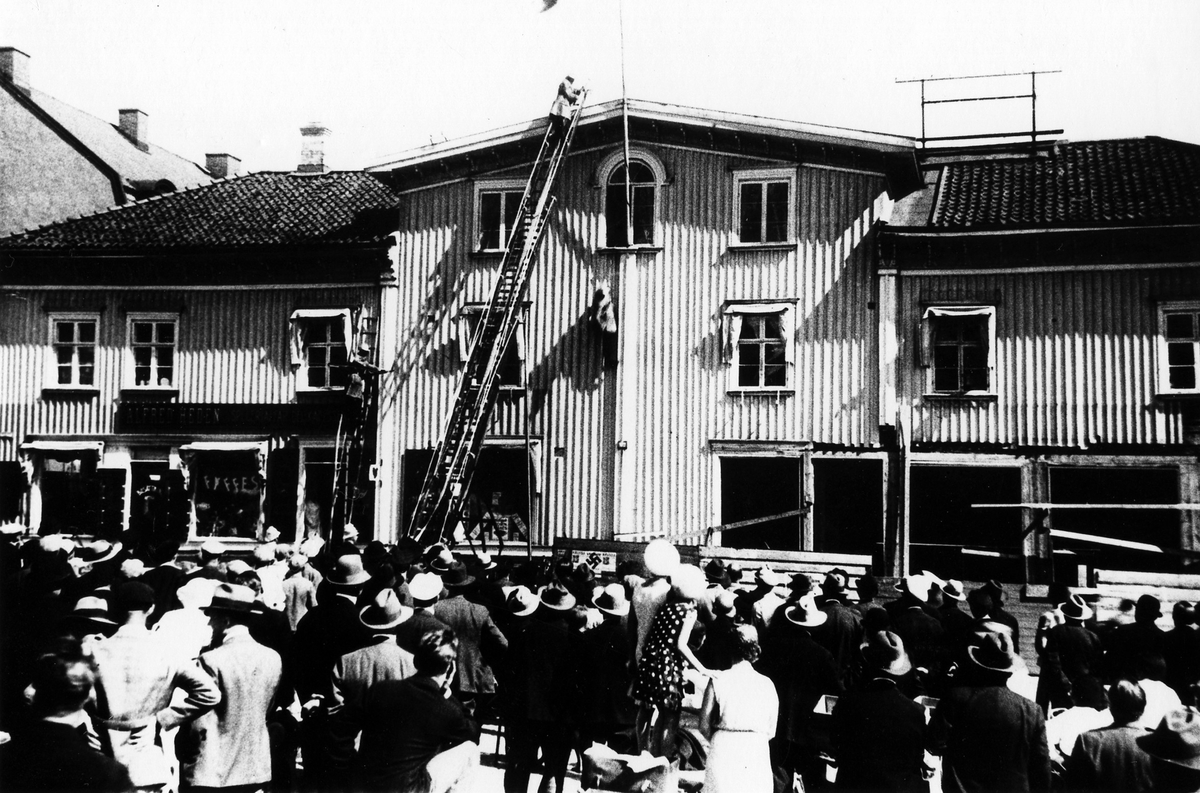 Brandövning i Hedénska fastigheten vid Stora torget, brandmän på stegar inför en folksamling.