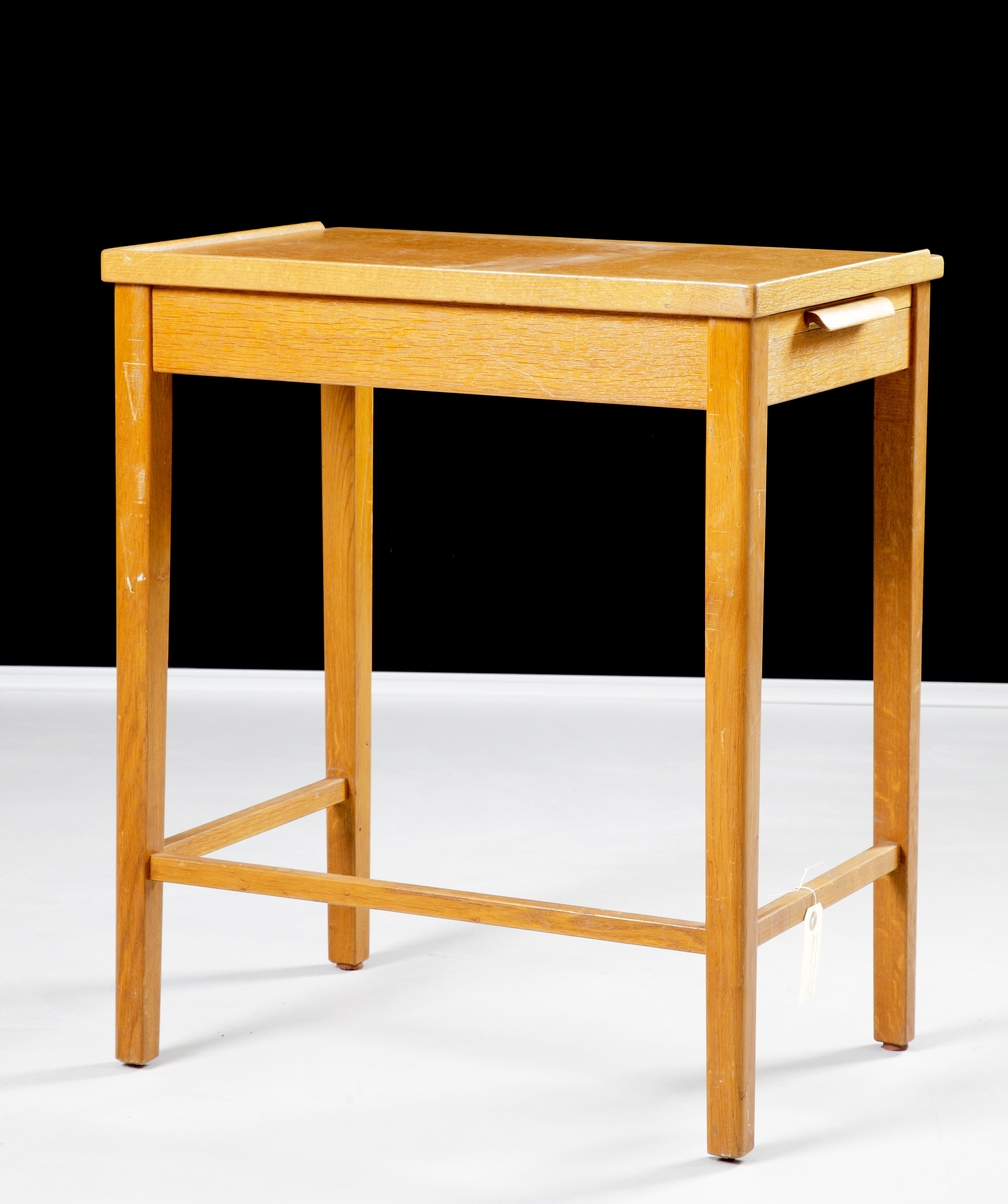 Ett rektangulärt, enkelt skrivmaskinsbord av fernissad ek och furu, på fyra ben. Utdragbara avlastningsskivor på var kortsida.