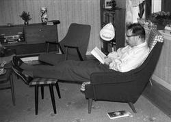 Mann leser en bok mens han sitter i en lenestol. Leiligheten