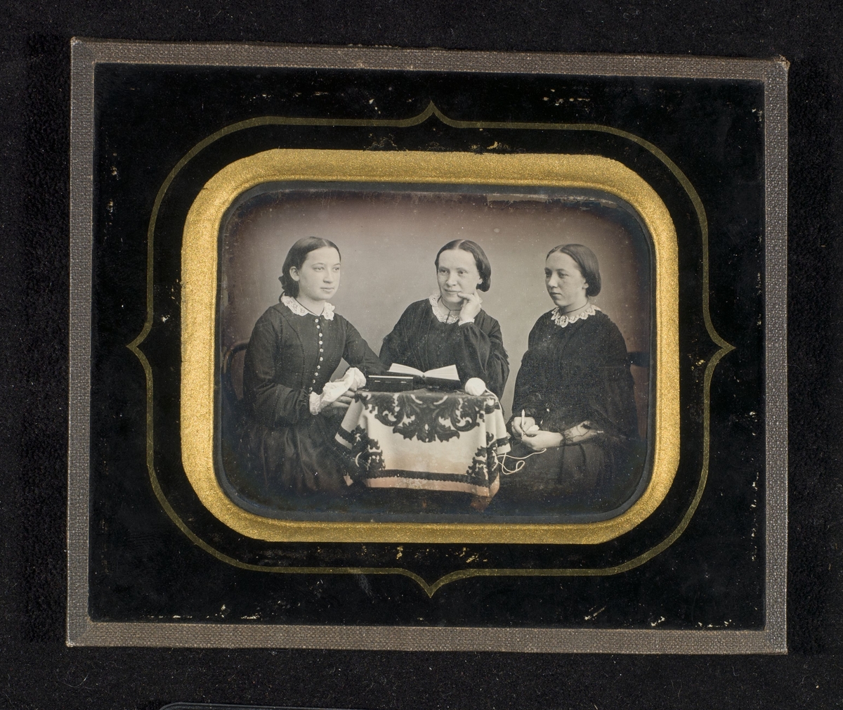 Daguerreotypi av tre unge kvinner som sitter ved et bord.